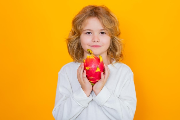 I bambini si affacciano con i frutti Il bambino tiene il frutto del drago in studio Studio ritratto di bambino carino con frutto del drago isolato su sfondo giallo spazio copia