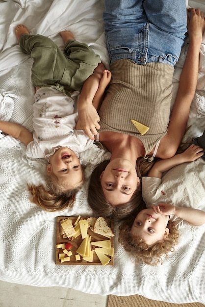 I bambini si sdraiano sul letto con la madre e mangiano pezzi di formaggio.