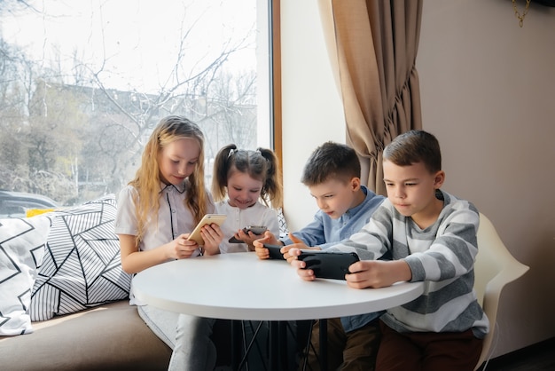 I bambini si siedono a un tavolo in un bar e giocano a telefoni cellulari insieme. Intrattenimento moderno.