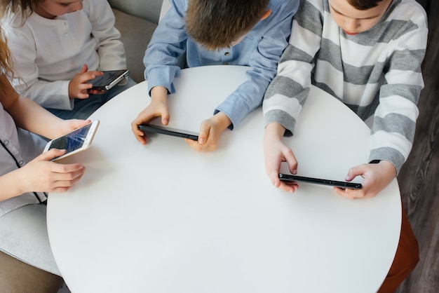 I bambini si siedono a un tavolo in un bar e giocano a telefoni cellulari insieme. Intrattenimento moderno.