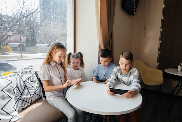 I bambini si siedono a un tavolo in un bar e giocano a telefoni cellulari insieme. Intrattenimento moderno.