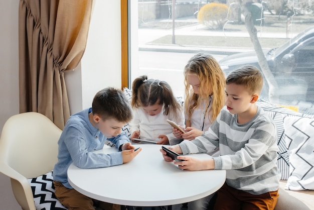 I bambini si siedono al tavolo del bar e giocano insieme ai telefoni cellulari.