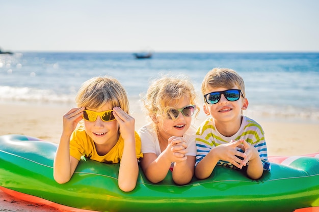 I bambini si siedono su un materasso gonfiabile in occhiali da sole contro il mare e si divertono