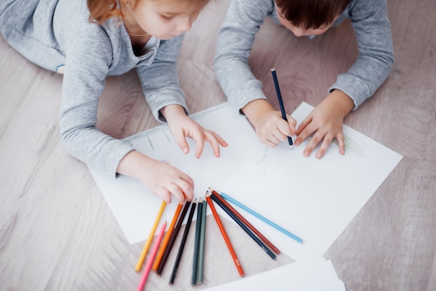 I bambini si trovano sul pavimento in pigiama e disegnano con le matite. Bambino carino dipinto di matite