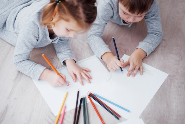 I bambini si trovano sul pavimento in pigiama e disegnano con le matite.