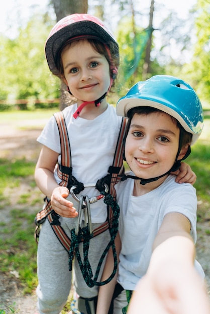 I bambini sorridenti e positivi sorridono, si fanno un selfie insieme. I bambini felici in marcia si divertono nel parco avventura rope