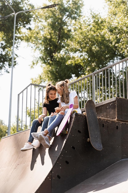 I bambini sportivi dipendenti dal telefono con skateboard e penny board usano i telefoni invece di pattinare e giocano insieme Bambini che guardano gli smartphone sulla rampa sportiva Bambini dipendenti dai telefoni