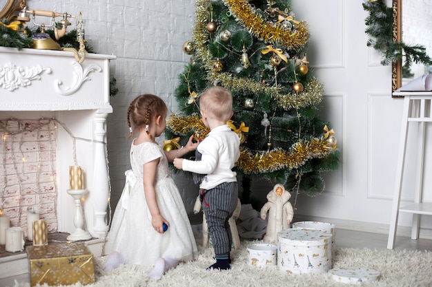 I bambini vicino all'albero di Natale, un ragazzo e una ragazza vestono l'albero di Natale