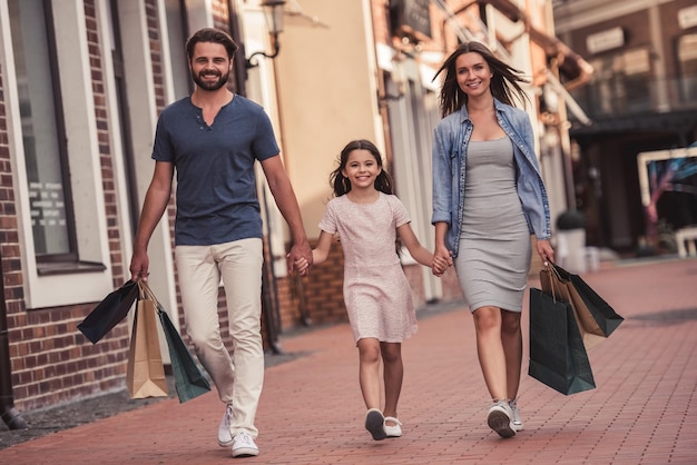 I bei genitori e la loro simpatica figlioletta portano borse della spesa, si tengono per mano e sorridono mentre camminano per strada