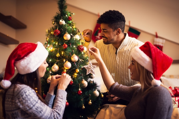 I bei giovani amici felici stanno decorando l'albero di Natale.