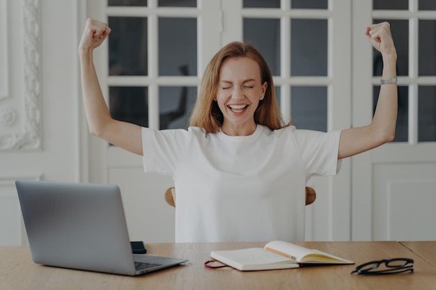 I bicipiti entusiasti dello spettacolo delle dipendenti celebrano le buone notizie alla scrivania con il laptop Successo