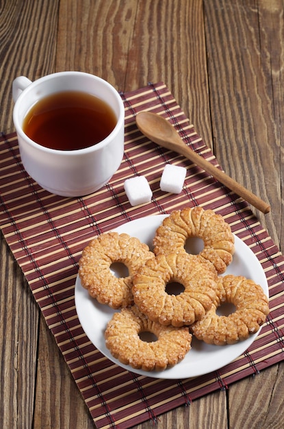 I biscotti di pasta frolla nel piatto e la tazza di tè su un tovagliolo di bambù si trovano sul tavolo di legno