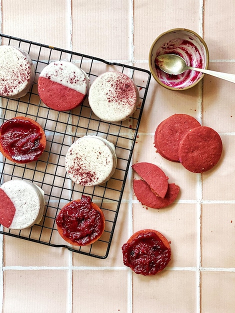 I biscotti di velluto rosso sono su una gratella accanto a un barattolo di marmellata.