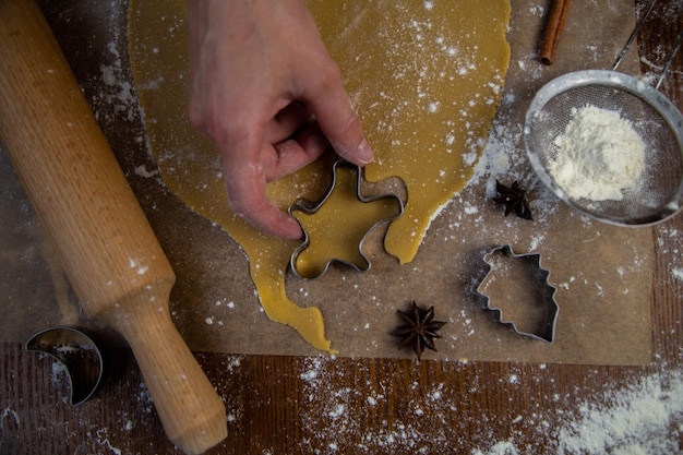 I biscotti vengono tagliati dalla pasta arrotolata sotto forma di un uomo la mano dei pasticceri tiene un biscotto cu...