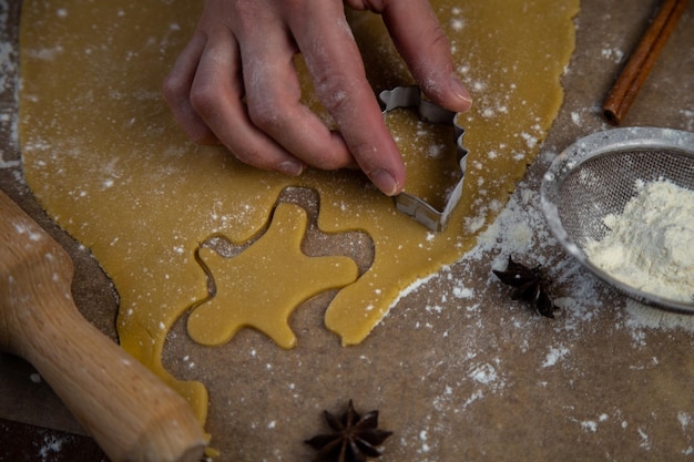 I biscotti vengono tagliati dalla pasta arrotolata sotto forma di un uomo la mano dei pasticceri tiene un biscotto cu...