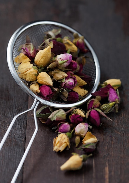 I boccioli di rosa mescolano il tè biologico nell'infusore del filtro su fondo di legno. macro
