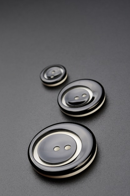 I bottoni in plastica per cucire sono disposti in fila sulla superficie nera.