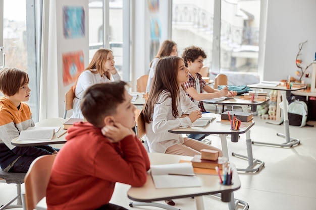 I bravi alunni ascoltano attentamente il loro tutor. Bambini delle scuole elementari seduti sulle scrivanie e leggere libri in classe.