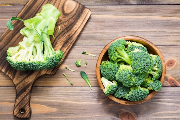 I broccoli crudi freschi pronti da mangiare sono divisi in infiorescenze in un piatto di legno e su un tagliere su un tavolo di legno.