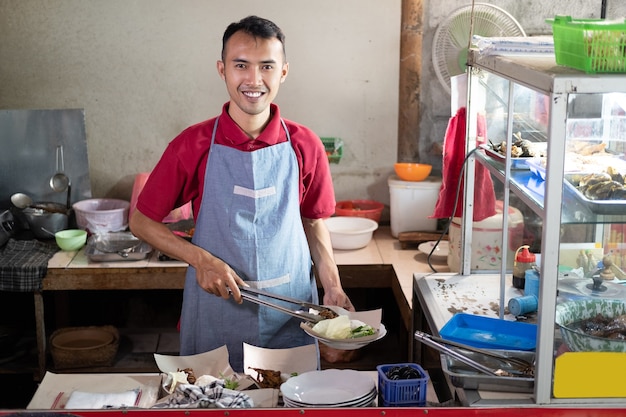 I camerieri asiatici stanno tenendo le pinze mentre preparano i contorni per gli ordini dei clienti alla bancarella