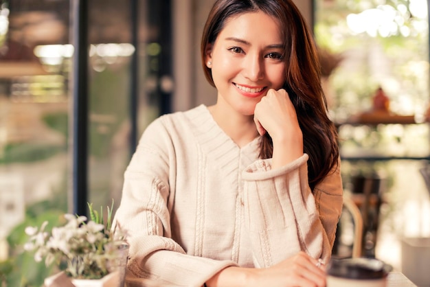 I capelli lunghi della bella donna asiatica sorridono e guardano la priorità bassa della caffetteria allegra e di felicità della macchina fotografica