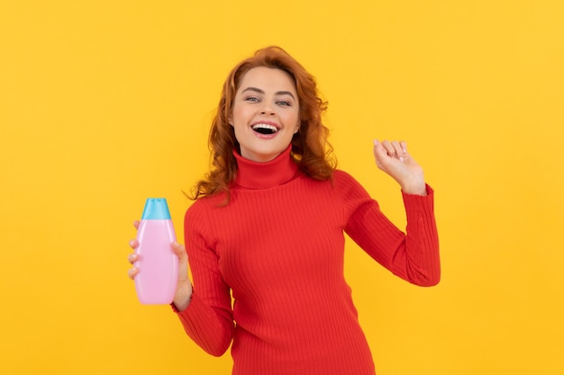 I capelli tinti ricci della signora rossa felice si divertono con il prodotto per la cura del corpo della bottiglia di shampoo antiforfora
