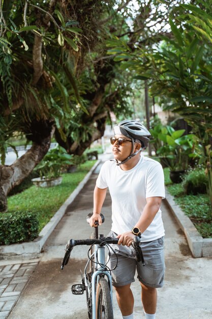 I caschi d'uso della bicicletta del giovane asiatico camminano in bici della via