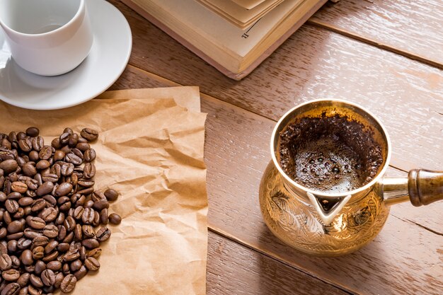 I chicchi di caffè arrostiti freschi in cezve (caffettiera turca tradizionale) hanno aperto il libro e la tazza sulla tavola di legno.