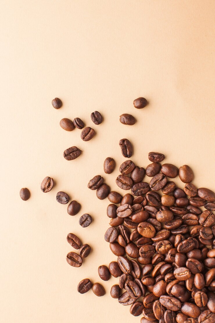 I chicchi di caffè in primo piano sono sparsi nell'angolo inferiore su uno sfondo marrone chiaro. Foto verticale con spazio per il testo. Per torrefattori, caffetterie e caffè.