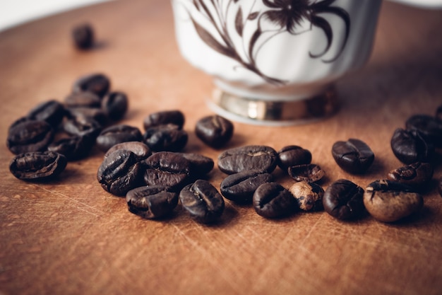 I chicchi di caffè si chiudono su una superficie di legno vicino alla tazza, messa a fuoco selettiva.