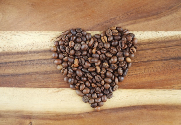 I chicchi di caffè sono disposti a forma di cuore su una tavola di legno Simbolo della vita