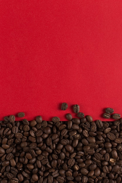 I chicchi di caffè sono sparsi su un primo piano di carta rosso, copyspace commerciale.