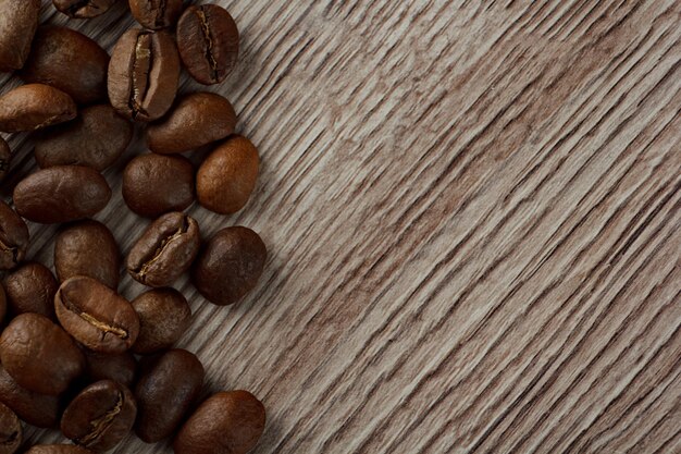 I chicchi di caffè sono sparsi su uno sfondo di legno dal bordo della cornice.