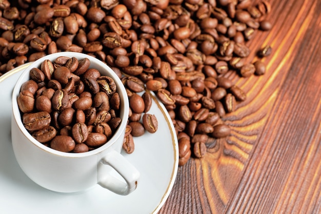 I chicchi di caffè tostati sono sparsi in tazza bianca e su legno marrone.