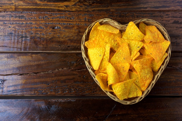 I chip di cereale dei nachos hanno messo la merce nel carrello con forma del cuore sulla tavola di legno, spazio per testo