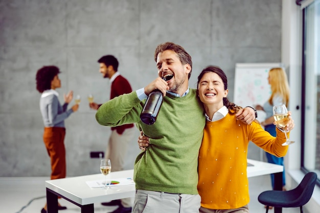 I colleghi alticci tengono lo champagne abbracciandosi cantando e celebrando la promozione e il successo