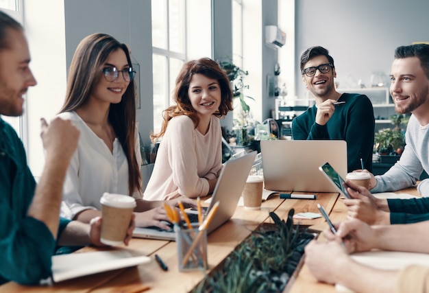 I colleghi diventano amici. Gruppo di giovani moderni in abbigliamento casual intelligente che discutono di qualcosa e sorridono mentre lavorano nell'ufficio creativo