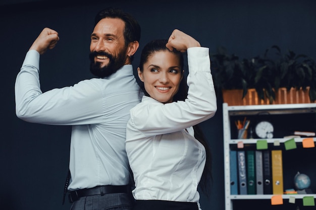 I colleghi maschi e femmine sorridenti dimostrano i muscoli