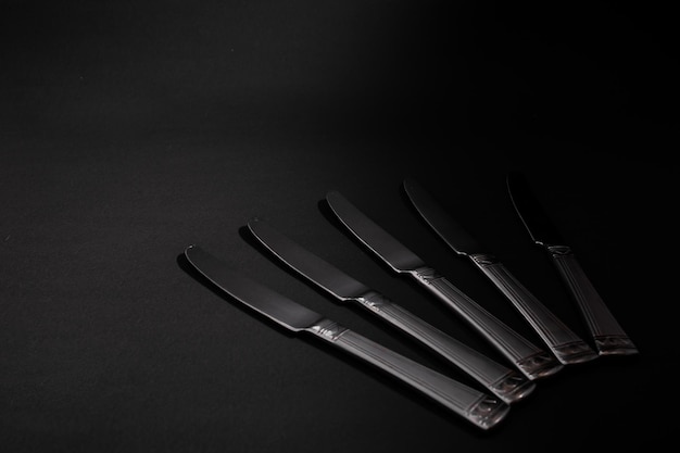 I coltelli in metallo, argento, giacciono su uno sfondo nero con un bagliore di luce