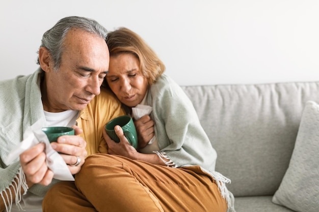 I coniugi anziani avvolti in una coperta con in mano tazze di tè o caffè caldo si sentono male e hanno freddo seduto