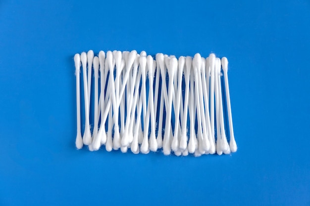I cotton fioc bianchi vengono raccolti uno accanto all'altro e giacciono al centro su uno sfondo blu.