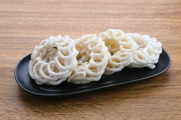 I cracker tradizionali di Krupuk o Kerupuk Indonesia sono serviti su un piatto nero su fondo di legno