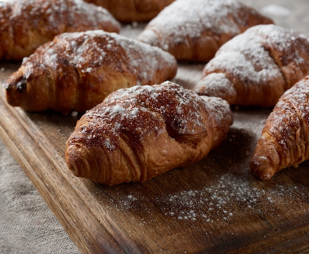 I croissant al forno cosparsi di zucchero a velo si trovano su una tavola di legno marrone, primi piani