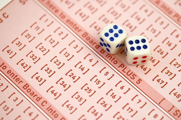 I dadi si trovano su fogli di gioco rosa con numeri per la marcatura per giocare alla lotteria Concetto di gioco della lotteria o dipendenza dal gioco Primo piano