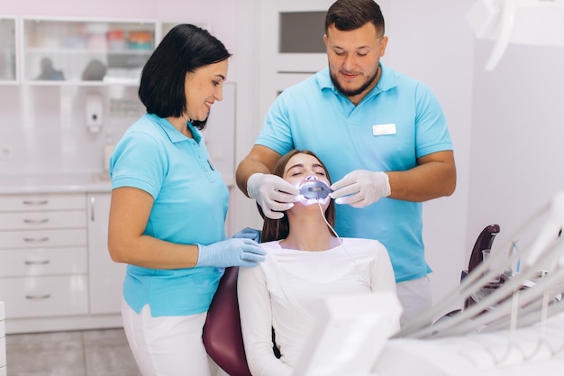 I dentisti danno alla ragazza lo sbiancamento dei denti a raggi ultravioletti in una clinica dentale