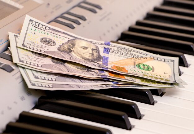 I dollari americani giacciono sui tasti del pianoforte. Pagamento per il concerto, profitto da esecuzione di opere musicali