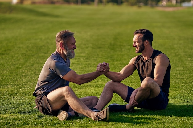 I due uomini felici seduti sull'erba e salutano