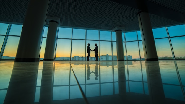 I due uomini si stringono la mano in ufficio sullo sfondo della finestra panoramica