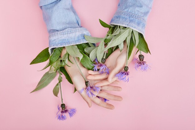 I fiori di campo dell'arte della mano alla moda crescono dalle donne dei cosmetici naturali delle maniche, i bellissimi fiori delle mani con il trucco a contrasto brillante, la cura delle mani. Foto di bellezza creativa ragazza seduta al tavolo, sfondo a contrasto