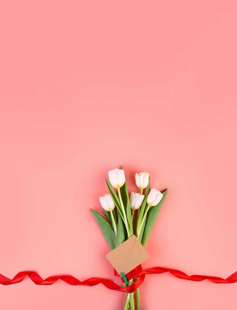 I fiori sono tulipani bianchi flatlay Un bel bouquet legato con un nastro rosso e una busta